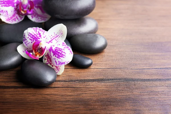 Ciottoli neri con orchidea su fondo di legno — Foto Stock