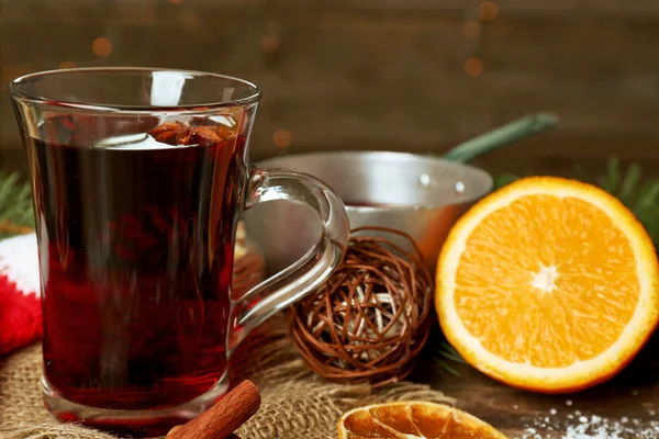 Christmas composition of mulled wine, cinnamon, pine and red knitted mittens on wooden table — Stock Photo, Image