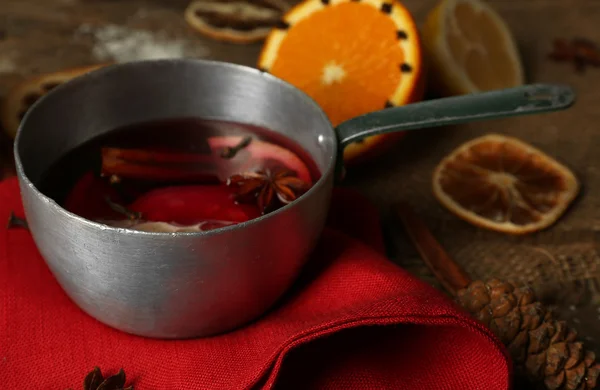 Mulled wine in stew-pan on decorated with red napkin, cinnamon and orange wooden background — Stock Photo, Image
