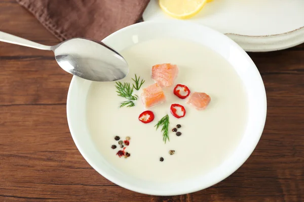 Delicious salmon cream soup with spoon on wooden table, close up — Stock Photo, Image