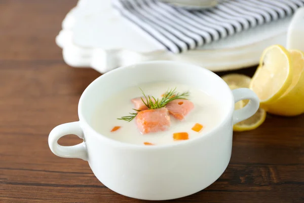 Delicious salmon cream soup in white bowl with lemon and striped cotton serviette on wooden table, close up — Stock Photo, Image