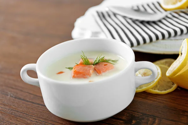 Heerlijke zalm crème soep in witte kom met citroen en gestreepte katoen servetring op houten tafel, close-up — Stockfoto