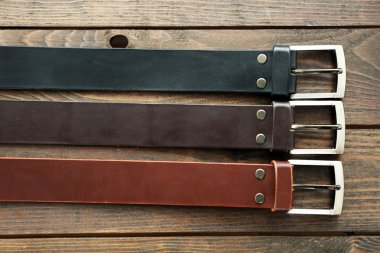 Leather belts with buckles on wooden background clipart