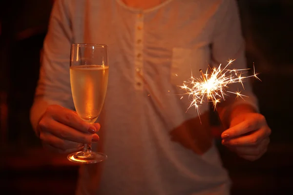 Female hands with sparkler and glass of sparkle wine on fireplace background — Stock Photo, Image