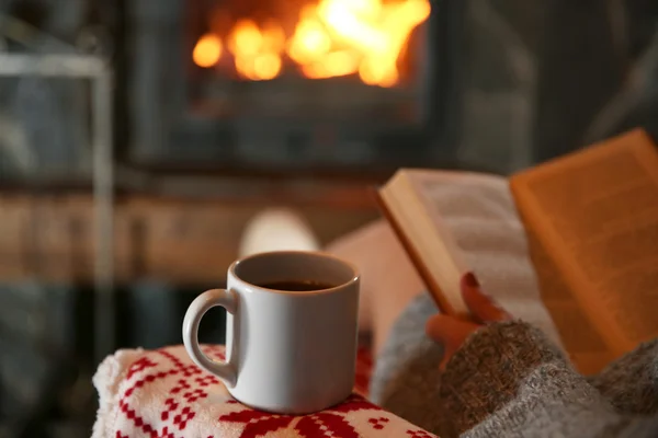 Donna a riposo con tazza di bevanda calda e libro vicino al camino — Foto Stock