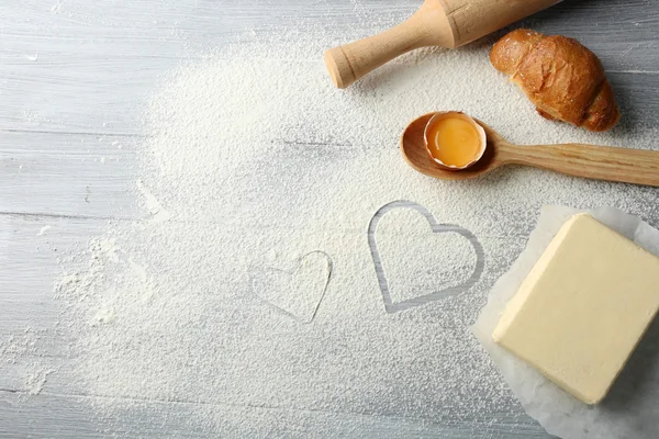 Coração de farinha, croissant e utensílios de cozinha de madeira em fundo cinza — Fotografia de Stock