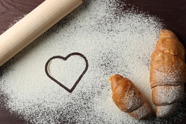 Corazón de harina, croissants y rodillo sobre fondo de mesa — Foto de Stock