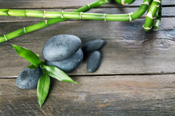 Piedras de spa y rama de bambú sobre fondo de madera —  Fotos de Stock