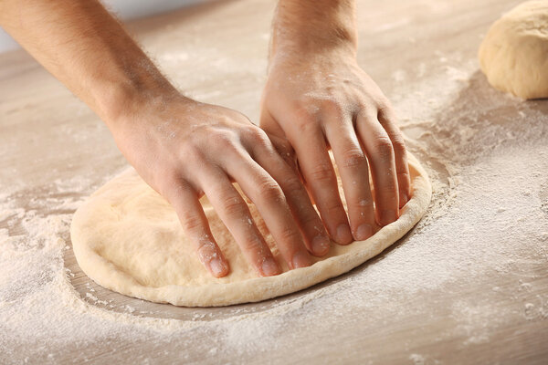 Hands preparing dough basis for pizza on the wooden table, close-up