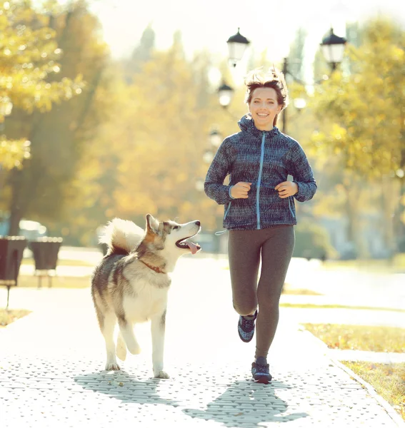 Счастливая молодая женщина бегает с собакой в парке — стоковое фото