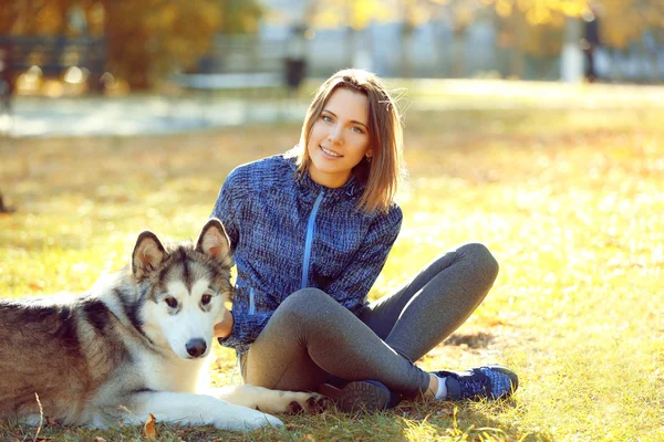 幸福的年轻女人和她的狗在公园的草地上坐着 — 图库照片
