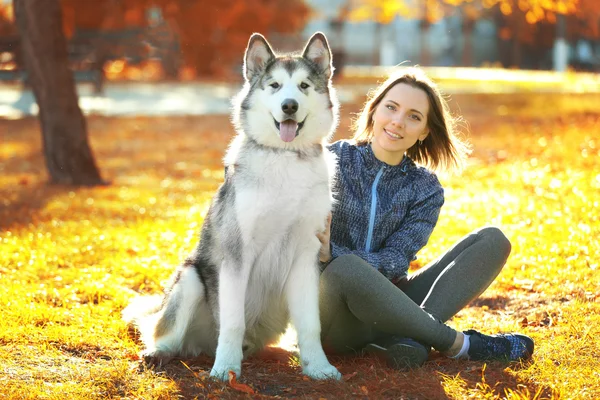 Szczęśliwa młoda kobieta siedzi z psem na trawie w parku — Zdjęcie stockowe