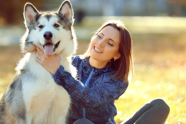 Happy young woman sitting with her dog on grass in park — Stock Photo, Image