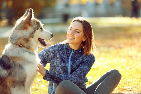 Gelukkig jonge vrouw zitten met haar hond op gras in park — Stockfoto