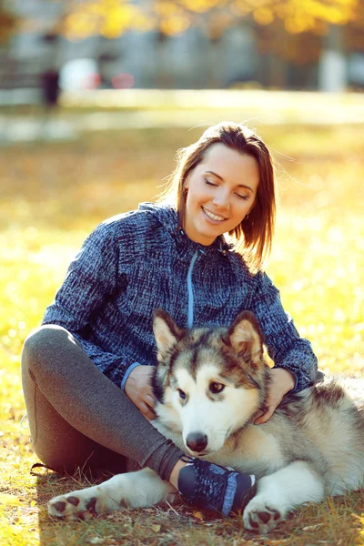 Happy young woman sitting with her dog on grass in park — Stock Photo, Image