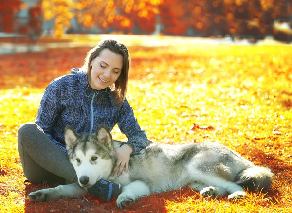 Feliz joven sentada con su perro en el césped en el parque — Foto de Stock