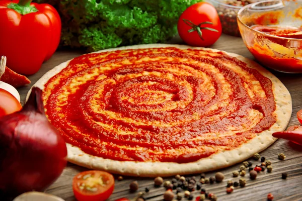 Teigbasis mit Ketchup und Zutaten für Pizza, auf dem Tisch — Stockfoto