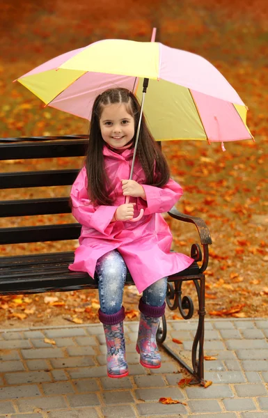 Gadis kecil yang cantik dengan payung duduk di bangku taman — Stok Foto