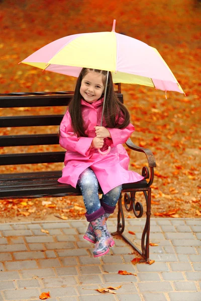 Bella bambina con ombrellone seduta su panchina nel parco — Foto Stock