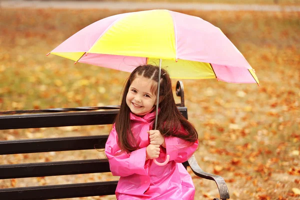 Beautiful little girl with umbrella sitting on bench in park — Stock Photo, Image