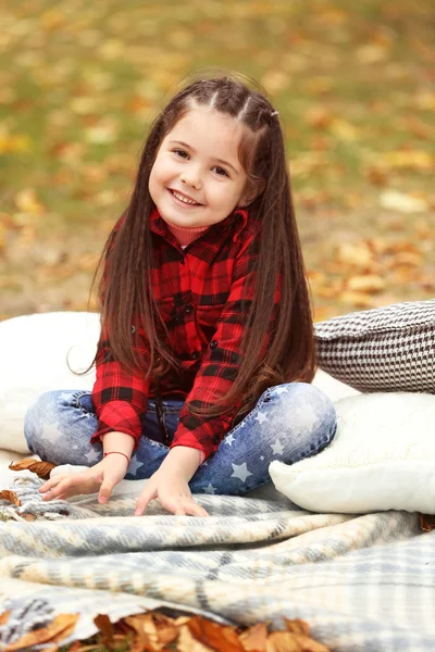 Ευτυχισμένη κοπέλα κάθεται σε καρό σε πάρκο φθινόπωρο — Φωτογραφία Αρχείου