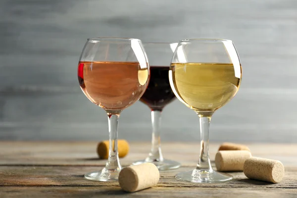 Composition of wine glasses and corks on wooden table against grey background — Stock Photo, Image