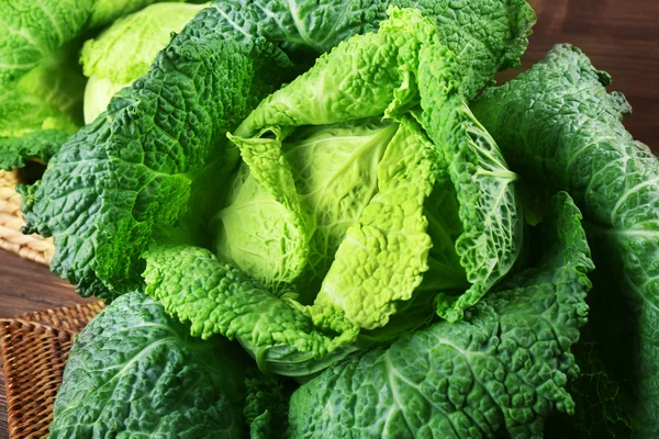 Savoy cabbage in wicker basket on wooden background, close up — Stock Photo, Image