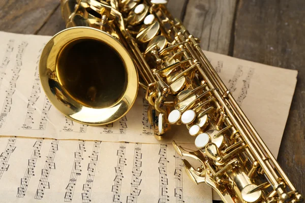 Beautiful golden saxophone with musical notes on wooden background, close up — Stock Photo, Image