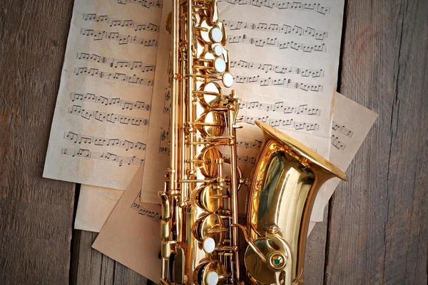 Wunderschönes goldenes Saxophon mit Noten auf Holzgrund, Nahaufnahme — Stockfoto
