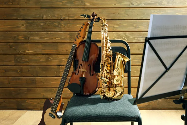 Instrumentos musicales sobre una silla y porta notas sobre fondo de madera —  Fotos de Stock