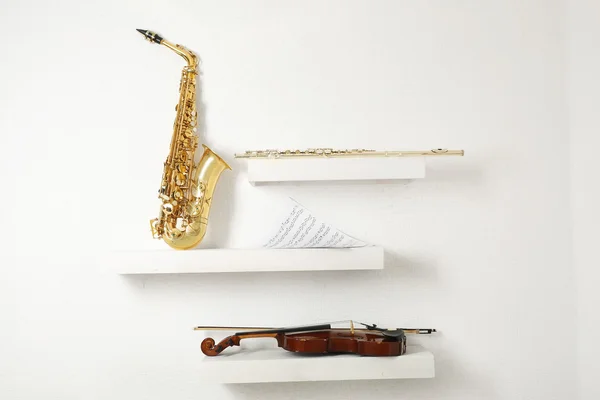 Скрипка, флейта и саксофон на украшенных полках на фоне белой стены — стоковое фото