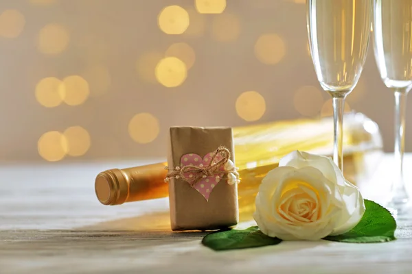 Bicchieri di vino, una bottiglia, una rosa bianca e un regalo nella scatola, su sfondo sfocato — Foto Stock
