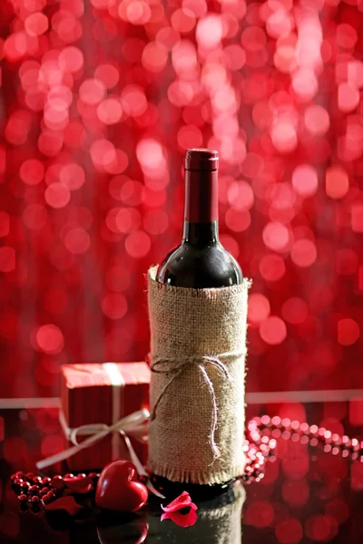 Ajuste de una botella de vino, un regalo en la caja y otra decoración, sobre fondo rojo borroso — Foto de Stock