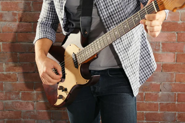 Young man playing guitar on brick wall background — Stock Photo, Image