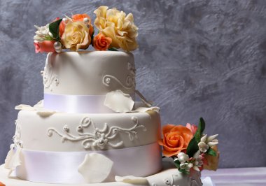 Gri zemin üzerine çiçeklerle süslenmiş beyaz düğün pastası