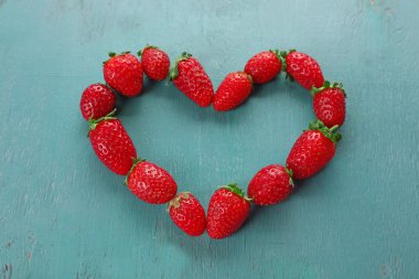 Çilek mavi ahşap arka plan üzerinde kalp şeklinde