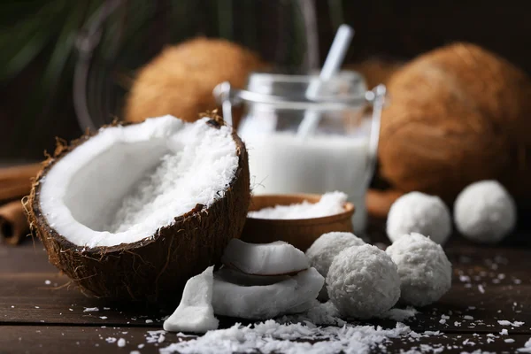 Caramelos en copos de coco, vaso de leche y coco fresco sobre fondo de madera oscura —  Fotos de Stock