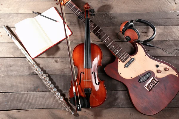 Chitarra elettrica, violino, sassofono soprano, cuffie e libro su sfondo di legno — Foto Stock