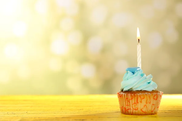 Sweet cupcake with candle on yellow wooden table against blurred background — Stock Photo, Image