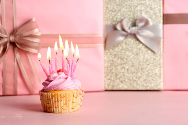 Sweet tasty cupcake with candles on pink present boxes background — Stock Photo, Image