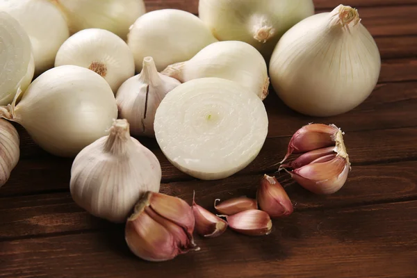 Frische ganze geschälte Zwiebeln mit Knoblauch auf Holzgrund — Stockfoto