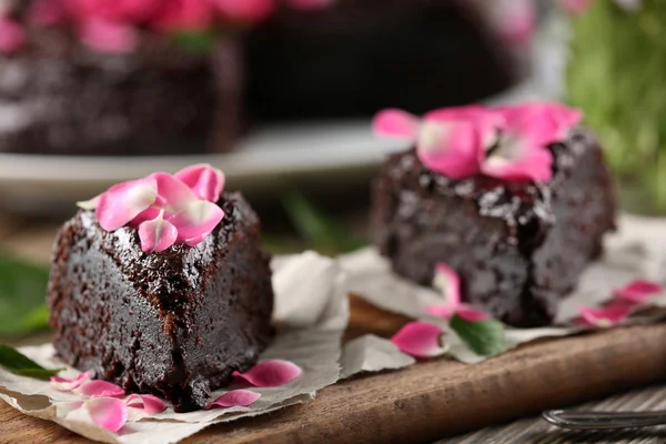 Piece of chocolate cake decorated with flowers on brown wooden table — Stock Photo, Image
