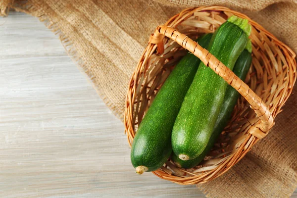 Frische Zucchini im Weidenkorb auf hölzernem Hintergrund — Stockfoto