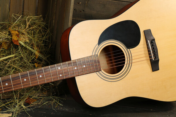 Acoustic guitar against box with hay on wooden background,, close up