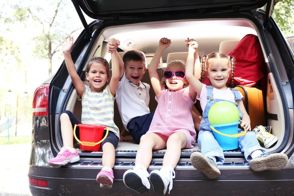 Три красивые девушки и мальчик сидят на багажнике машины и смеются — стоковое фото