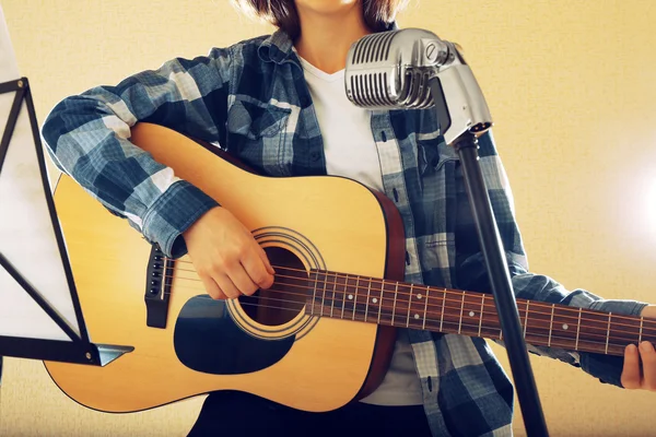 Músico toca la guitarra en estudio de luz con soporte de notas musicales, de cerca — Foto de Stock