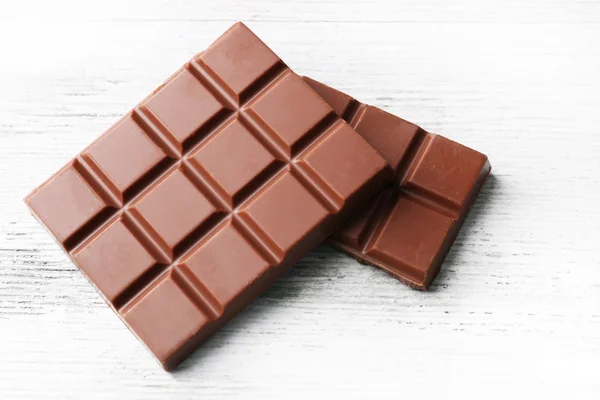 Pedaços de chocolate de leite na cor de fundo de madeira — Fotografia de Stock
