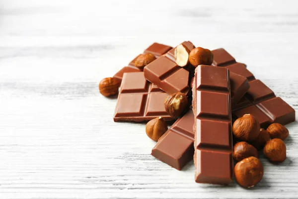 Chocolate pieces with nuts on color wooden background — Stock Photo, Image