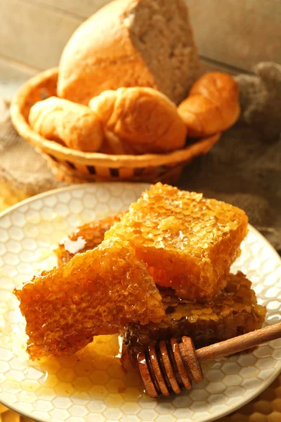 Waben auf Teller, heiße Brötchen im Korb auf Holzgrund — Stockfoto