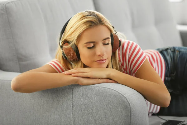 Mujer joven en un sofá escuchando música — Foto de Stock